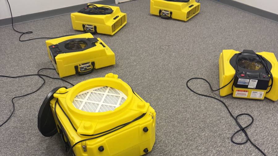 Air movers and a dehumidifier set up to dry a carpeted commercial room